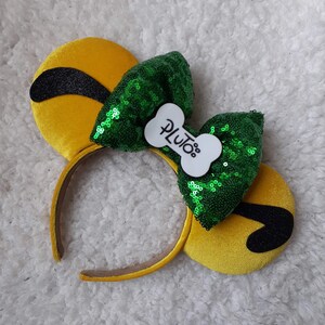 May include: Yellow mouse ears headband with a green sequin bow and a white bone-shaped tag that says "Pluto".
