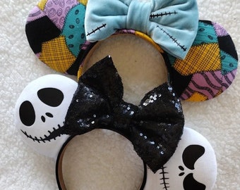May include: Two pairs of character-themed headbands. One headband features ears with a yellow, purple, and teal patchwork pattern and a light blue bow with black stitch details. The other headband has white ears with black facial features and a black sequined bow.