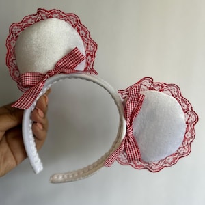 May include: White headband with red and white gingham bows and red lace trim. The headband is designed to look like mouse ears.