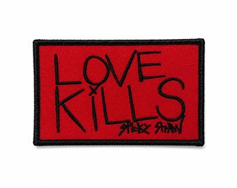 Puede incluir: Un parche rectangular rojo con las palabras "LOVE KILLS" en letras negras estilizadas. El parche tiene un borde negro y el nombre "STACY SHAW" está escrito debajo.