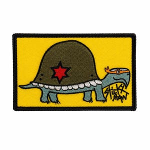 May include: Embroidered patch featuring a cartoon turtle with a green shell and a red star. The turtle has a blue body and an orange mask. The patch is on a yellow background with the text "STICKY RAW".