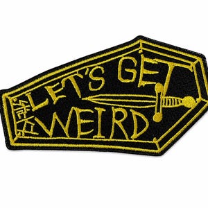 Puede incluir: Parche negro en forma de ataúd con texto bordado amarillo y un diseño de espada. El texto dice "LET'S GET WEIRD" en una fuente juguetona, con texto adicional en una fuente estilizada en el lado izquierdo. El parche tiene un borde amarillo.