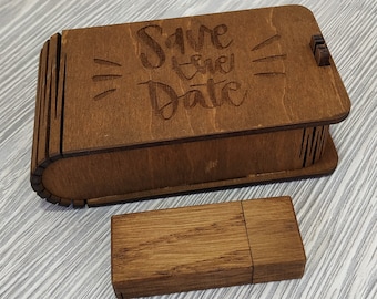 May include: A wooden box with a hinged lid and the text "Save the Date" engraved on the front. The box is sitting on a light wood surface. A small wooden USB drive is also pictured.