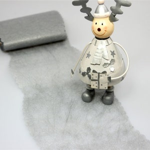 Könnte beinhalten: Eine skurrile Weihnachtsdekoration mit einem Rentier mit silbernen Hörnern, Hut und Stiefeln. Daneben ein rechteckiges silbernes Objekt und eine Spur aus silbernem Material, die eine festliche Szene erzeugt.
