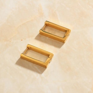 May include: A pair of gold-toned rectangular hoop earrings. The earrings are simple and modern in design.