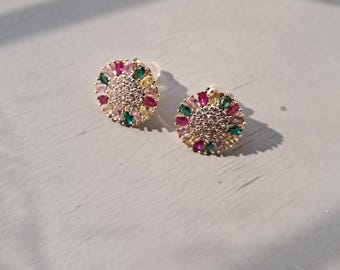 May include: A pair of gold-toned stud earrings. Each earring features a circular design with a central cluster of small, clear stones surrounded by colorful, teardrop-shaped gems in pink, green, and yellow.