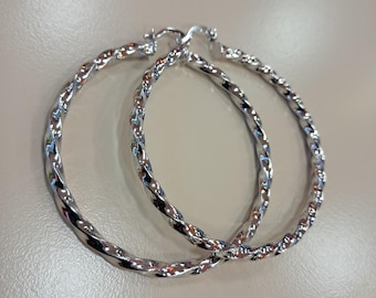 May include: A pair of silver-colored hoop earrings with a twisted rope design. The earrings are circular and have a shiny, reflective surface. The hoops are shown against a neutral background.