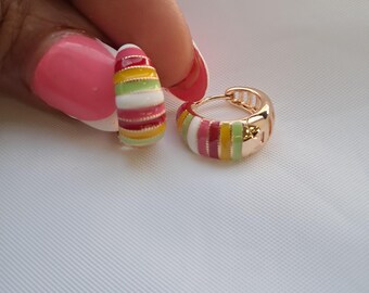 May include: A pair of small hoop earrings featuring a gold-tone metal base with horizontal enamel stripes in alternating colors of white, light green, yellow, and dark pink. The earrings have a hinged closure mechanism for secure fastening.