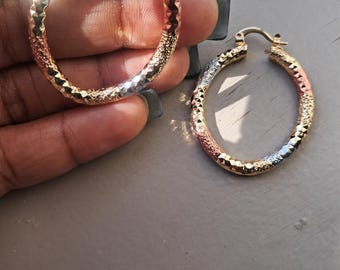 May include: A pair of tri-color hoop earrings featuring a textured, diamond-cut surface. The hoops are crafted with alternating segments of yellow, rose, and white metal tones, each displaying a faceted finish that catches the light.
