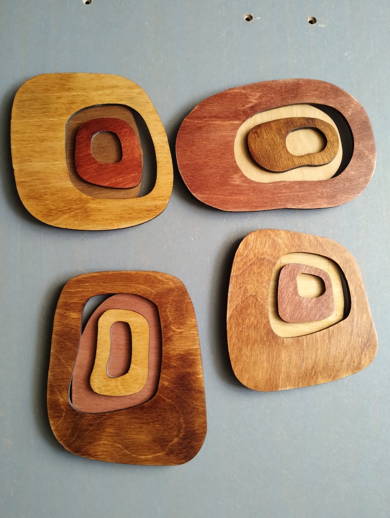 Op de afbeelding: Vier houten wanddecoraties in de vorm van afgeronde rechthoeken met concentrische cirkels die zijn uitgesneden. De stukken zijn gebeitst in tinten bruin, rood en beige.