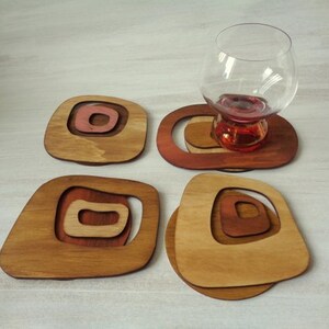Op de afbeelding: Set van vier houten onderzetters met een geometrisch ontwerp. Elke onderzetter heeft concentrische cirkels in tinten bruin en rood.