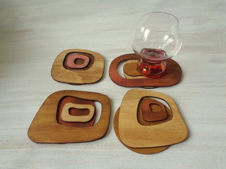 Op de afbeelding: Set van vier houten onderzetters met een geometrisch ontwerp. Elke onderzetter heeft concentrische cirkels in tinten bruin en rood.