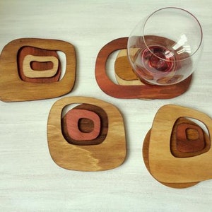 Op de afbeelding: Vier houten onderzetters met een geometrisch ontwerp in tinten bruin en rood. De onderzetters zijn gemaakt van hout en hebben een unieke, moderne uitstraling.
