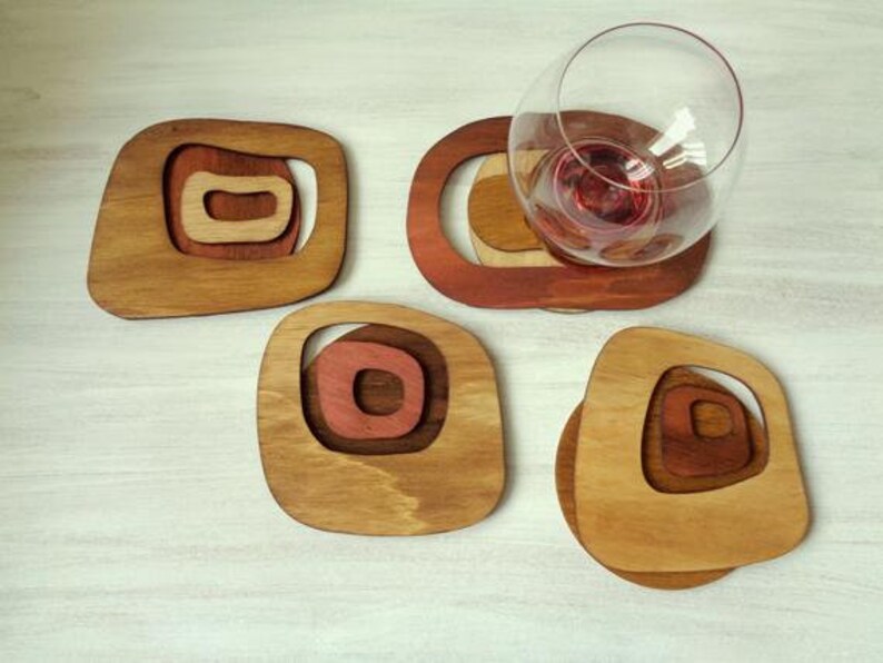 Op de afbeelding: Vier houten onderzetters met een geometrisch ontwerp in tinten bruin en rood. De onderzetters zijn gemaakt van hout en hebben een unieke, moderne uitstraling.