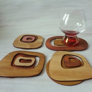 Op de afbeelding: Set van vier houten onderzetters met een geometrisch ontwerp in tinten bruin en roze. De onderzetters zijn gemaakt van hout en hebben een unieke, moderne uitstraling.