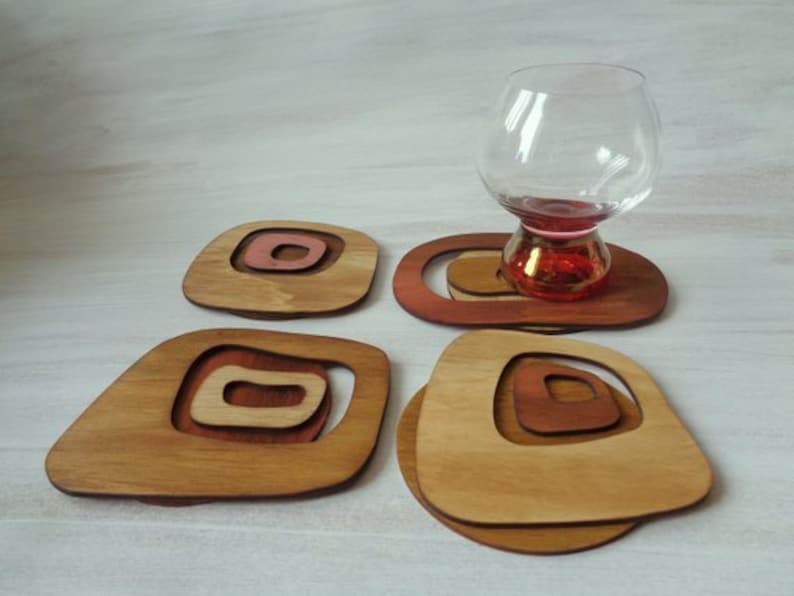 Op de afbeelding: Set van vier houten onderzetters met een geometrisch ontwerp in tinten bruin en roze. De onderzetters zijn gemaakt van hout en hebben een unieke, moderne uitstraling.