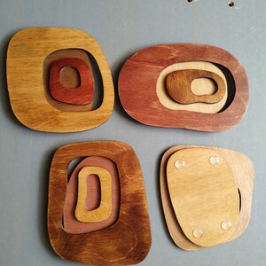 Op de afbeelding: Vier houten wanddecoraties in verschillende tinten bruin en rood. Elk stuk heeft een concentrisch cirkelontwerp met een uitsparing in het midden.