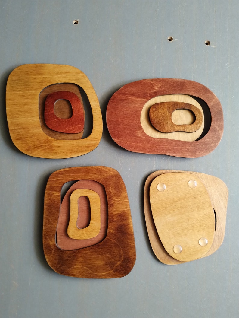 Op de afbeelding: Vier houten wanddecoraties in verschillende tinten bruin en rood. Elk stuk heeft een concentrisch cirkelontwerp met een uitsparing in het midden.