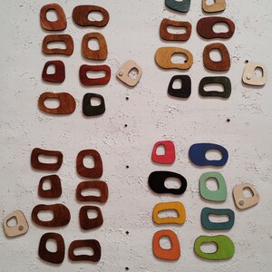 Op de afbeelding: Een verzameling houten vormen in verschillende kleuren en maten, waaronder rood, groen, blauw, geel en bruin. De vormen zijn gerangschikt in een rasterpatroon op een witte, getextureerde achtergrond.