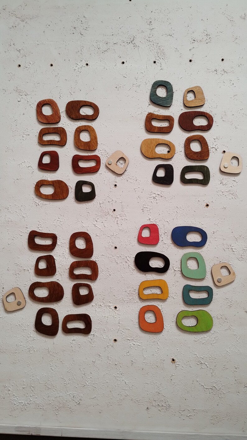 Op de afbeelding: Een verzameling houten vormen in verschillende kleuren en maten, waaronder rood, groen, blauw, geel en bruin. De vormen zijn gerangschikt in een rasterpatroon op een witte, getextureerde achtergrond.