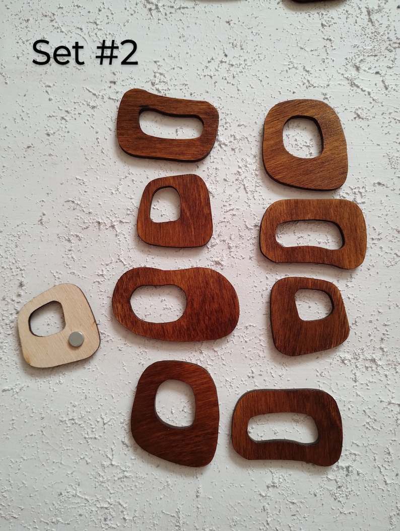 Op de afbeelding: Set van tien houten vormen met uitgesneden ontwerpen. De vormen zijn in verschillende maten en hebben een donkerbruine vlek. De tekst "Set #2" is zichtbaar in de linkerbovenhoek van de afbeelding.