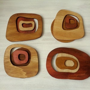 Op de afbeelding: Vier houten onderzetters met een geometrisch ontwerp. Elke onderzetter heeft concentrische cirkels in tinten bruin, rood en beige.