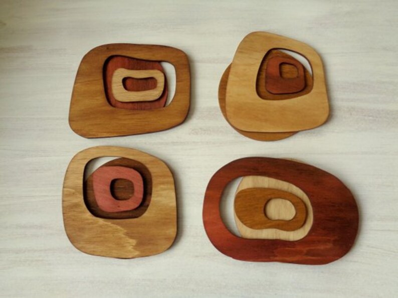Op de afbeelding: Vier houten onderzetters met een geometrisch ontwerp. Elke onderzetter heeft concentrische cirkels in tinten bruin, rood en beige.