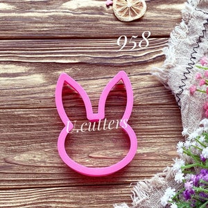 May include: Pink plastic bunny cookie cutter on a wooden background. The cutter is shaped like a bunny head with long ears. The number 958 is visible in the top right corner of the image.