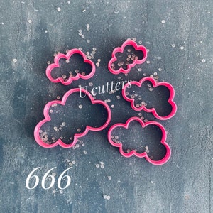 Puede incluir: Cinco cortadores de galletas en forma de nube de color rosa sobre un fondo gris con cuentas blancas esparcidas a su alrededor. El texto "666" es visible en la esquina inferior izquierda de la imagen.