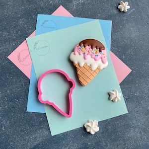 Könnte beinhalten: Rosa-weißer Eiswaffel-Ausstecher mit brauner Schokoladen-Topping und Streuseln. Der Ausstecher liegt auf einem hellblauen Hintergrund mit einem rosa Hintergrund dahinter. Der Text "U.Cutters" ist auf dem Hintergrund sichtbar.