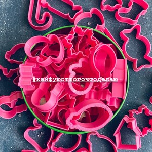 K&ouml;nnte beinhalten: Ein Set rosa Plastik-Ausstecher in einer gr&uuml;nen Dose. Die Ausstecher sind in Form von Weihnachtsb&auml;umen, Sternen, Zuckerstangen, Schneem&auml;nnern und anderen weihnachtlichen Formen. Der Text #кайфуюоттогочтоделаю ist auf der Dose sichtbar.