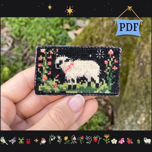 May include: A small, rectangular cross-stitch design showing a white sheep with a pink collar, surrounded by red flowers and green foliage against a black background. The design is held in a hand. The word "PDF" is in a blue banner.