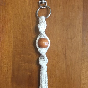 May include: A white macrame keychain with a brown wooden bead and a silver metal key ring.
