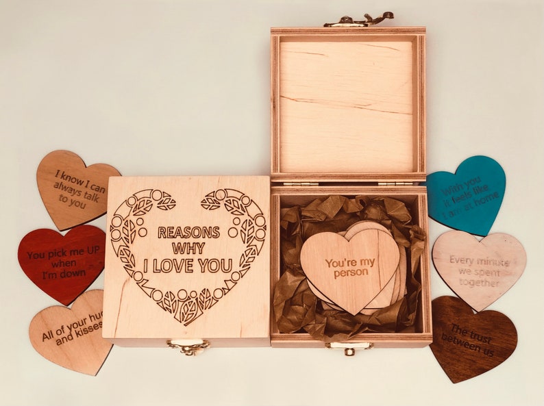 以下が含まれることがあります： 「REASONS WHY I LOVE YOU」の文字が蓋に刻まれた木製のボックスセット。ボックスには「You're my person」などのフレーズが書かれたハート型の木製カードが入っています。愛のメッセージが書かれたハート型のカードがいくつか散らばっています。