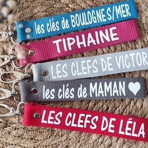 Peut inclure: Cinq porte-clés colorés avec du texte blanc. Les porte-clés sont en tissu et ont un anneau en métal. Le texte sur les porte-clés est : "les clés de BOULOGNE S/MER", "TIPHAINE", "LES CLEFS DE VICTOR", "les clés de MAMAN", et "LES CLEFS DE LÉLA".