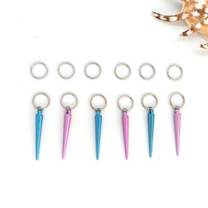 K&ouml;nnte beinhalten: Sieben silberne Sprungringe mit sechs daran befestigten Metallspitzen in Blau und Rosa. Die Spitzen sind spitz und haben eine metallische Oberfl&auml;che.