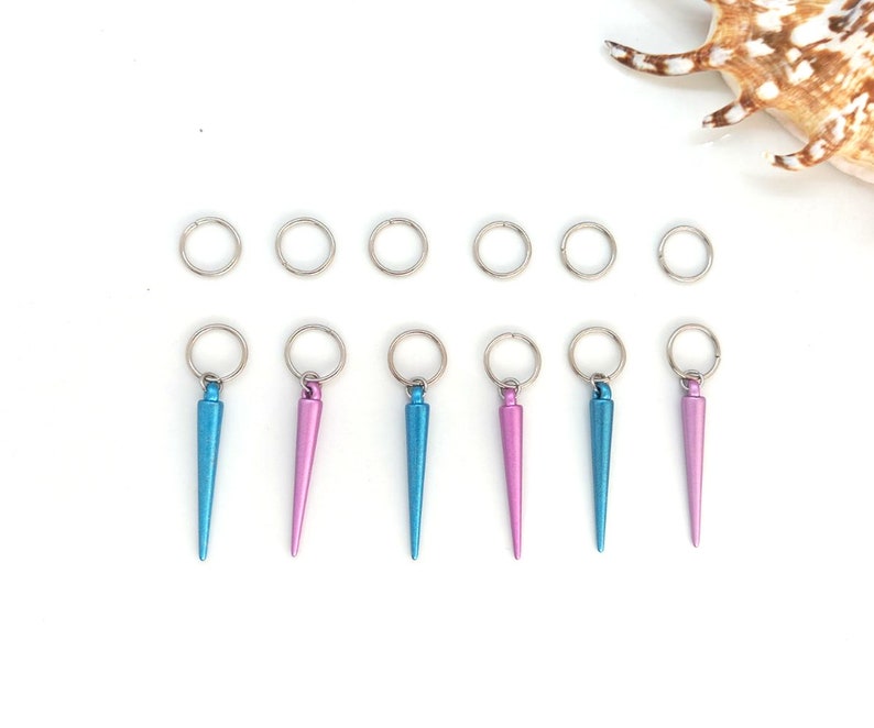 K&ouml;nnte beinhalten: Sieben silberne Sprungringe mit sechs daran befestigten Metallspitzen in Blau und Rosa. Die Spitzen sind spitz und haben eine metallische Oberfl&auml;che.