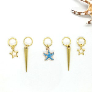 K&ouml;nnte beinhalten: F&uuml;nf goldfarbene Haarschmuckst&uuml;cke mit verschiedenen Designs. Die Charms beinhalten einen Stern, einen Stern mit blauer Mitte, eine Spitze und zwei Sterne.