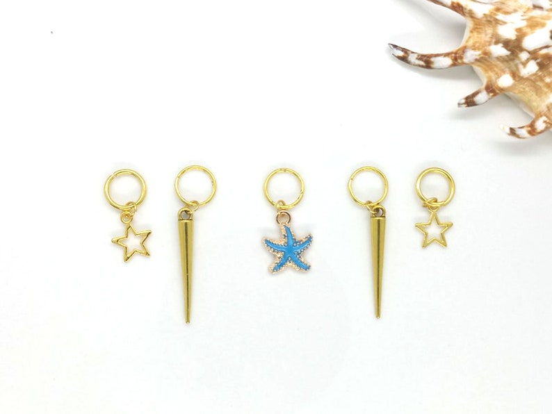K&ouml;nnte beinhalten: F&uuml;nf goldfarbene Haarschmuckst&uuml;cke mit verschiedenen Designs. Die Charms beinhalten einen Stern, einen Stern mit blauer Mitte, eine Spitze und zwei Sterne.