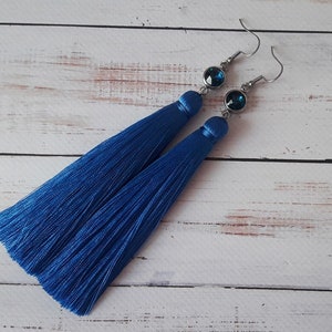 Peut inclure: Une paire de longues boucles d'oreilles en forme de pompon bleu avec un accent de cristal bleu foncé sur chaque boucle d'oreille.