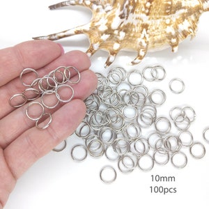May include: A pile of 100 silver jump rings, each measuring 10mm in diameter. The rings are scattered on a white surface.
