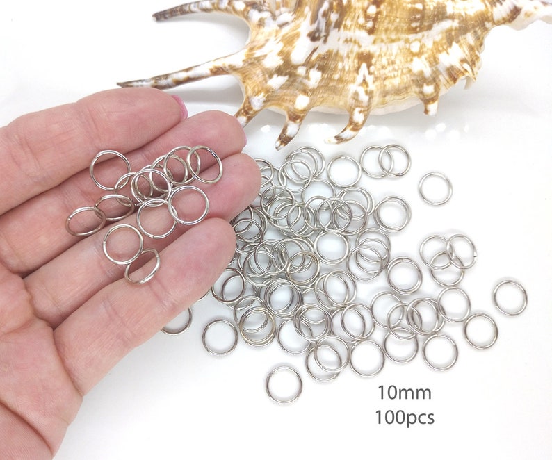 May include: A pile of 100 silver jump rings, each measuring 10mm in diameter. The rings are scattered on a white surface.