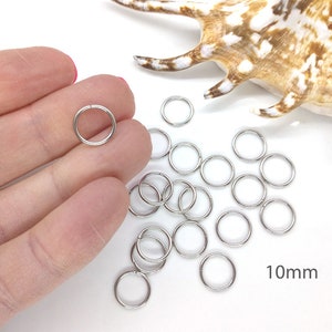 May include: A pile of silver jump rings, 10mm in diameter, on a white surface. The rings are used for jewelry making and crafting.