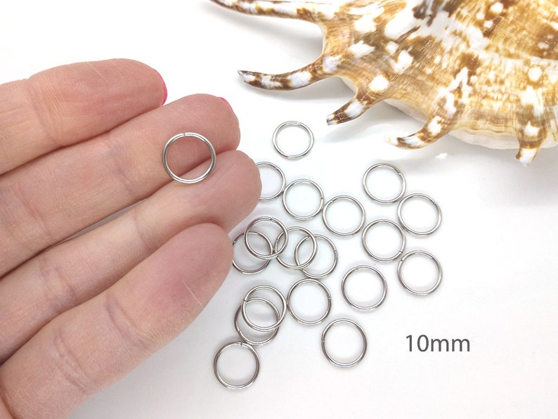 May include: A pile of silver jump rings, 10mm in diameter, on a white surface. The rings are used for jewelry making and crafting.