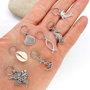 May include: A set of seven silver hair tie charms with various sea-themed designs, including a seashell, a fish, a seahorse, a dolphin, an anchor, and a cross.