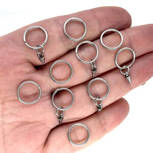 K&ouml;nnte beinhalten: Zehn silberne Schl&uuml;sselringe mit einem kleinen silbernen konischen Anh&auml;nger an jedem Ring.