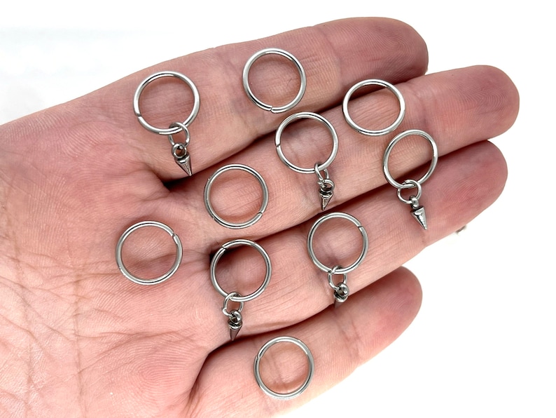 K&ouml;nnte beinhalten: Zehn silberne Schl&uuml;sselringe mit einem kleinen silbernen konischen Anh&auml;nger an jedem Ring.