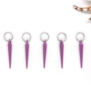 K&ouml;nnte beinhalten: F&uuml;nf violette Metall-Haargummi-Anh&auml;nger mit einer spitzen Spitze und einem silbernen Ring.