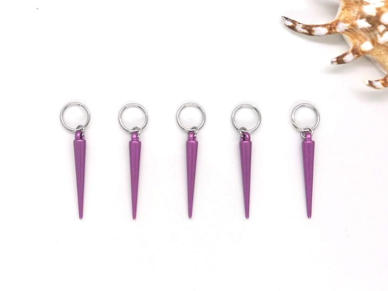 K&ouml;nnte beinhalten: F&uuml;nf violette Metall-Haargummi-Anh&auml;nger mit einer spitzen Spitze und einem silbernen Ring.