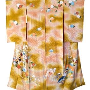 Könnte beinhalten: Ein traditioneller japanischer Kimono in Gold-, Pfirsich- und Weißtönen, verziert mit Blumen- und Vogelmotiven. Das Kleidungsstück hat lange Ärmel und ein Wickeldesign mit detaillierten Stickereien und einem zarten Muster. Der Kimono hängt an einem Kleiderbügel.